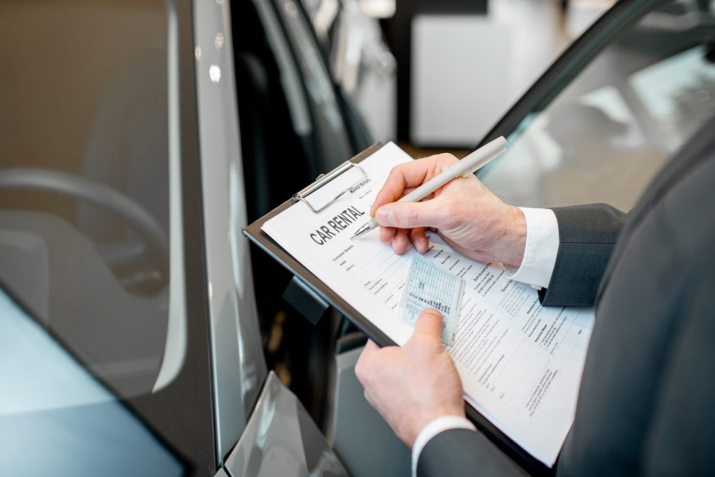 Manager filling car rental documents holding folder with driver license in the showroom with car on the background